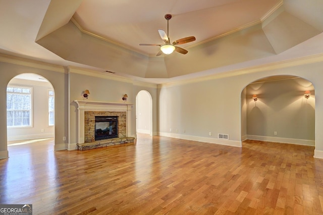 unfurnished living room featuring visible vents, a tray ceiling, crown molding, a stone fireplace, and light wood-style floors