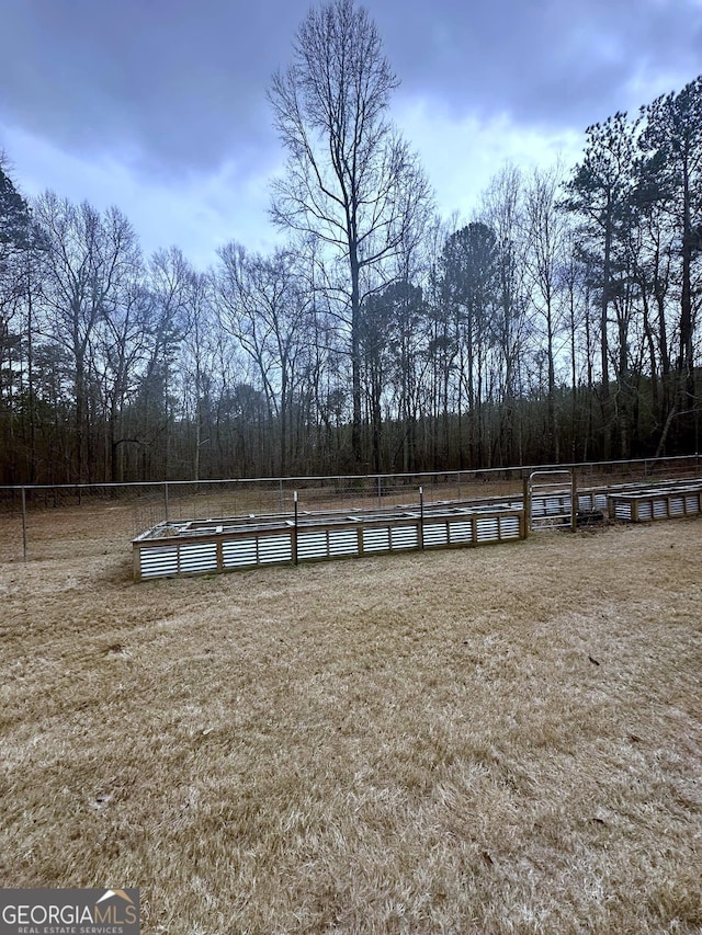 view of yard featuring a rural view, an enclosed area, a wooded view, and fence