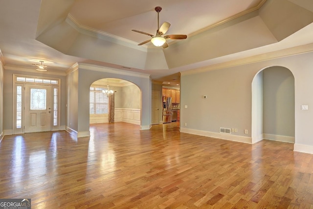 entryway with arched walkways, light wood-style flooring, visible vents, a raised ceiling, and crown molding