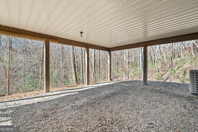 view of patio with central air condition unit, a wooded view, and a carport