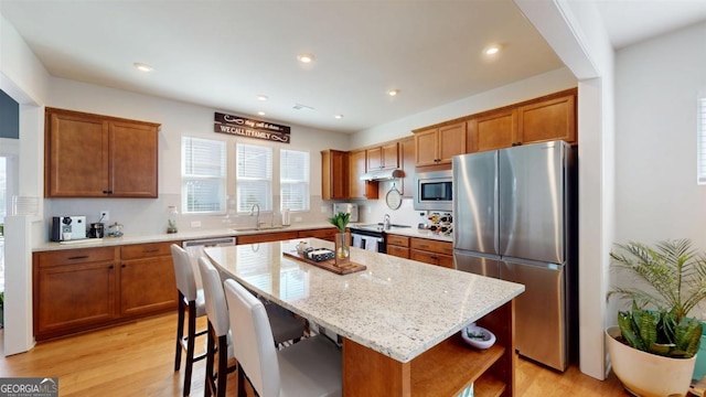 kitchen with appliances with stainless steel finishes, sink, light stone counters, a center island, and light wood-type flooring