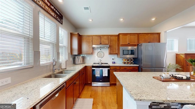 kitchen with sink, appliances with stainless steel finishes, light stone countertops, and light hardwood / wood-style floors