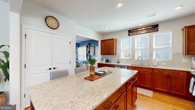 kitchen featuring light hardwood / wood-style flooring, sink, light stone counters, a center island, and decorative backsplash