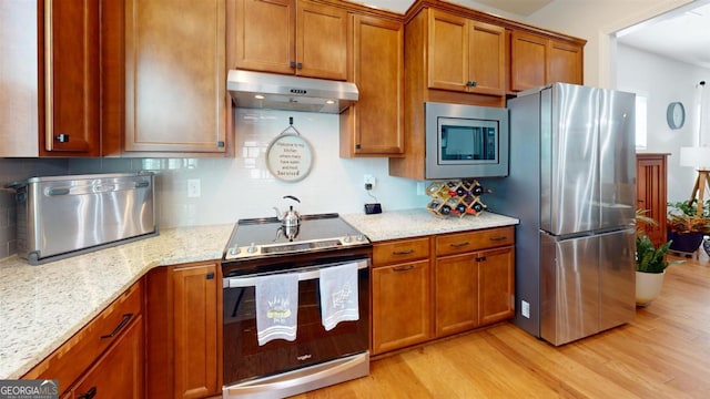 kitchen with tasteful backsplash, light stone countertops, stainless steel appliances, and light hardwood / wood-style floors