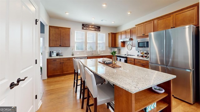 kitchen featuring a kitchen island, light stone countertops, sink, appliances with stainless steel finishes, and a kitchen breakfast bar