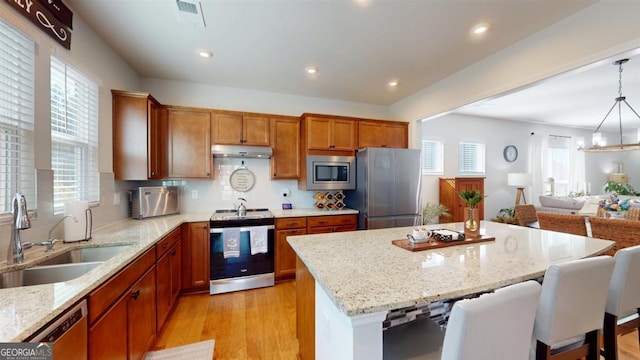 kitchen featuring stainless steel appliances, sink, light stone counters, a breakfast bar area, and pendant lighting