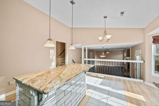 kitchen with ceiling fan with notable chandelier, light wood-type flooring, pendant lighting, and a textured ceiling