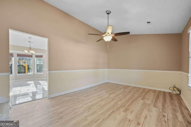 spare room featuring ceiling fan with notable chandelier, light hardwood / wood-style floors, and lofted ceiling