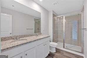 full bathroom with double vanity, toilet, a sink, a shower stall, and wood finished floors