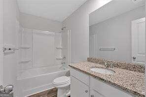 bathroom featuring  shower combination, toilet, wood finished floors, and vanity