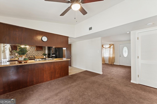 kitchen featuring stainless steel gas cooktop, kitchen peninsula, light colored carpet, backsplash, and black fridge