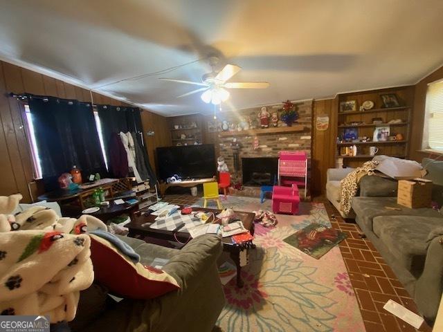 living room featuring a brick fireplace, wood walls, and ceiling fan