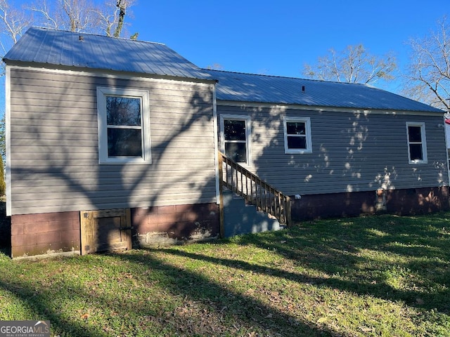 back of house with entry steps, metal roof, and a yard