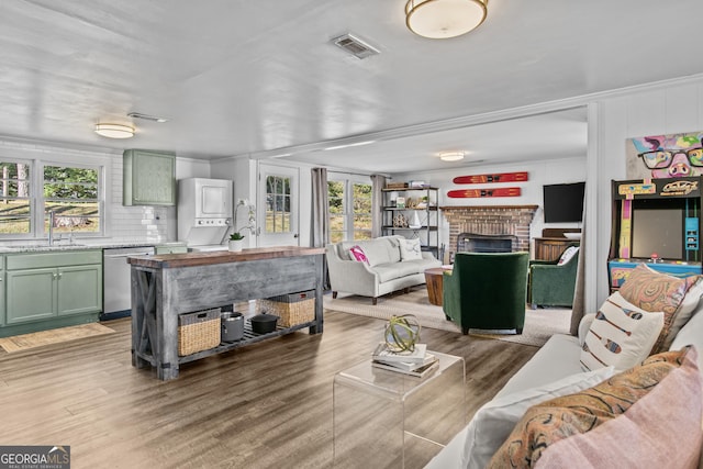 living room featuring hardwood / wood-style floors, stacked washer and clothes dryer, a brick fireplace, and sink