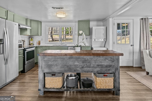 kitchen with appliances with stainless steel finishes, sink, stacked washer / drying machine, and green cabinetry