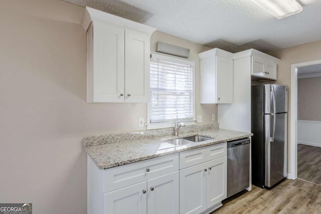 kitchen with light stone countertops, light hardwood / wood-style floors, sink, appliances with stainless steel finishes, and white cabinets