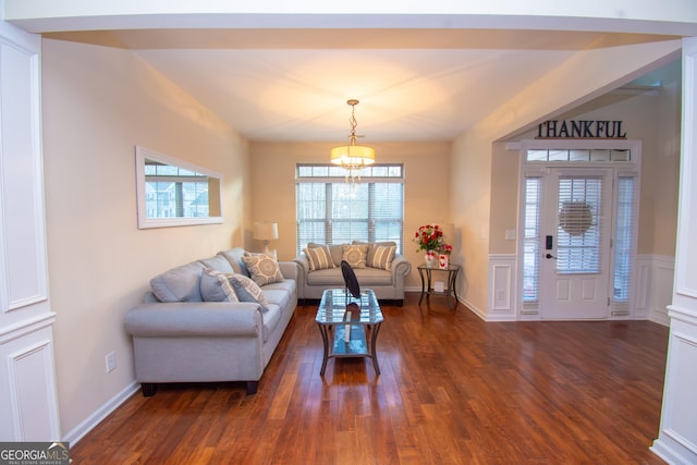 living area featuring dark wood-style floors, wainscoting, a decorative wall, and an inviting chandelier