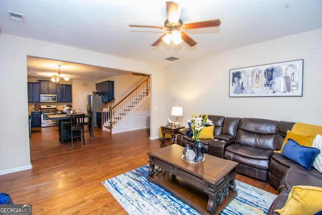 living room with ceiling fan with notable chandelier, visible vents, stairway, and wood finished floors