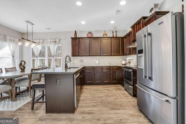 kitchen featuring appliances with stainless steel finishes, hanging light fixtures, light stone countertops, sink, and a kitchen bar