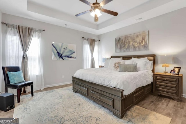 bedroom featuring light wood-type flooring, a tray ceiling, and ceiling fan