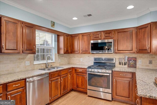 kitchen featuring visible vents, a sink, light stone counters, light wood-style floors, and appliances with stainless steel finishes