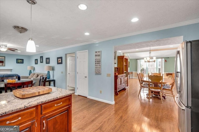 kitchen with brown cabinetry, a textured ceiling, freestanding refrigerator, and light wood-style floors