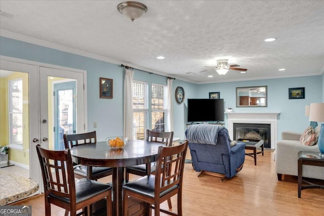 dining space with a glass covered fireplace, light wood-style floors, visible vents, and ornamental molding