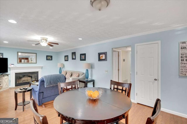 dining area with crown molding, baseboards, light wood-type flooring, a glass covered fireplace, and a textured ceiling