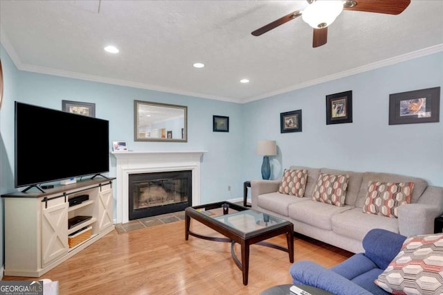 living area featuring light wood-type flooring, a fireplace with flush hearth, a textured ceiling, recessed lighting, and crown molding
