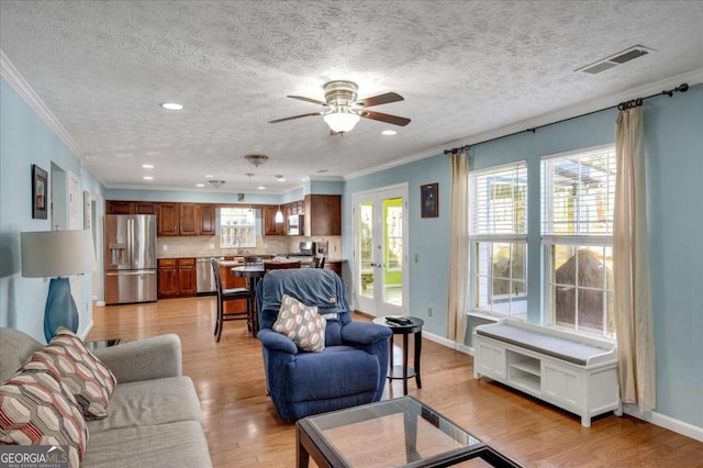 living room with light wood-type flooring, visible vents, baseboards, and ornamental molding