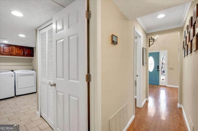 hallway featuring visible vents, light wood-type flooring, ornamental molding, washer and dryer, and a textured ceiling