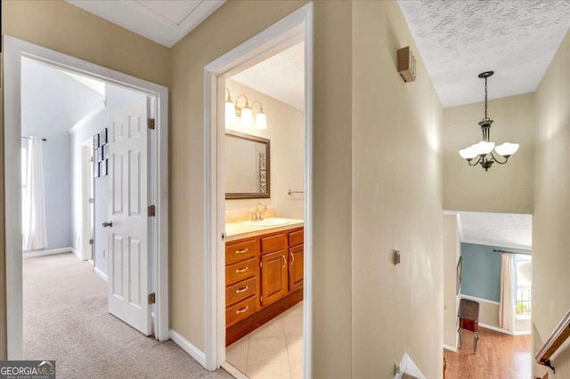 hall with a notable chandelier, a sink, a textured ceiling, baseboards, and light colored carpet