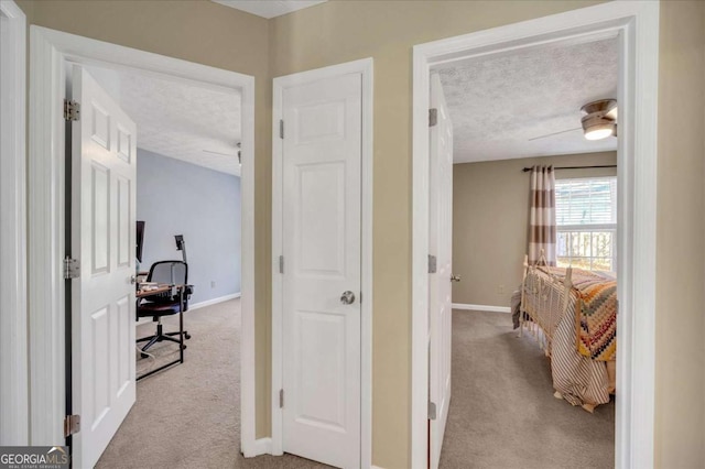 corridor featuring baseboards, light colored carpet, and a textured ceiling
