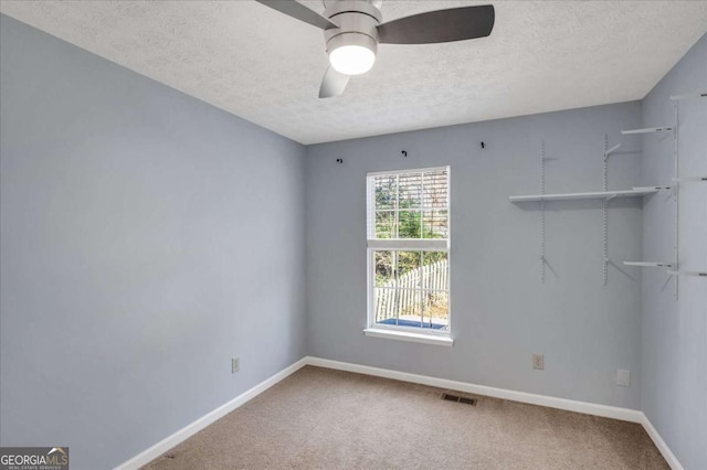 carpeted empty room featuring a ceiling fan, baseboards, visible vents, and a textured ceiling