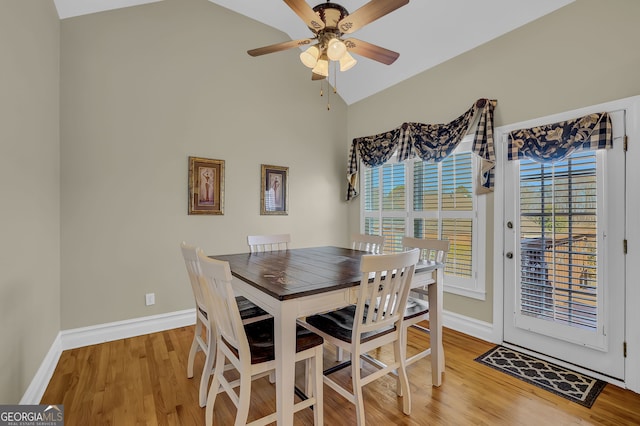 dining space featuring a ceiling fan, light wood-type flooring, vaulted ceiling, and baseboards