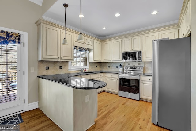 kitchen featuring dark countertops, light wood-style flooring, a peninsula, stainless steel appliances, and a sink