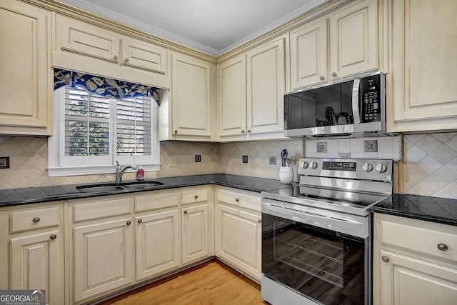 kitchen with light wood finished floors, stainless steel appliances, backsplash, cream cabinets, and a sink