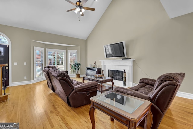 living room with baseboards, high vaulted ceiling, a tiled fireplace, and light wood-style floors