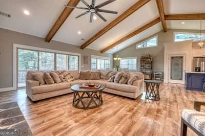 living room featuring high vaulted ceiling, beamed ceiling, light hardwood / wood-style floors, and ceiling fan with notable chandelier