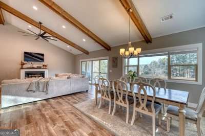 dining room with ceiling fan with notable chandelier, lofted ceiling with beams, and wood-type flooring