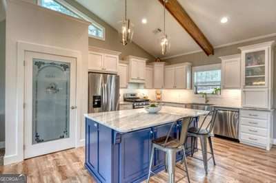 kitchen featuring appliances with stainless steel finishes, white cabinetry, vaulted ceiling with beams, and decorative light fixtures