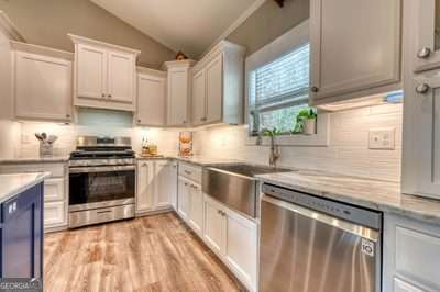 kitchen with vaulted ceiling, light wood-type flooring, white cabinetry, stainless steel appliances, and tasteful backsplash