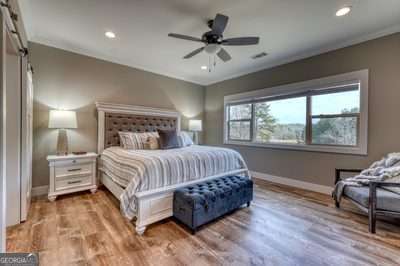 bedroom with hardwood / wood-style flooring, a barn door, crown molding, and ceiling fan