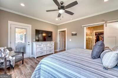 bedroom with ornamental molding, a barn door, ceiling fan, and light hardwood / wood-style flooring