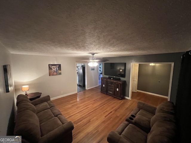 living area with ceiling fan, a textured ceiling, baseboards, and wood finished floors