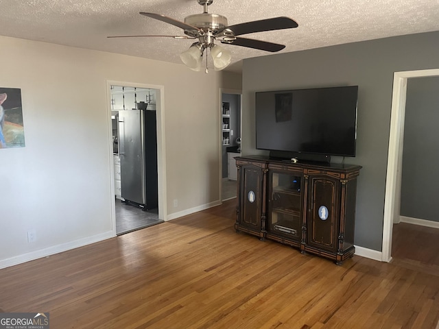 living area with ceiling fan, a textured ceiling, baseboards, and wood finished floors