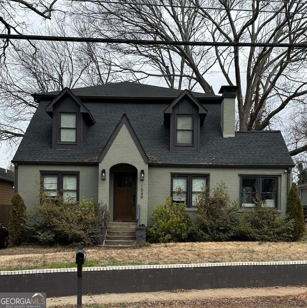 view of front facade with brick siding, a chimney, and roof with shingles