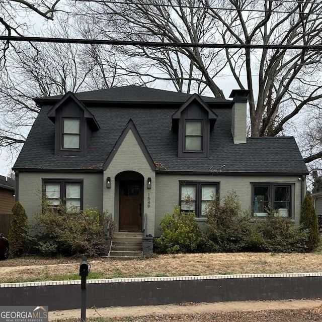 view of front facade with brick siding, a chimney, and roof with shingles