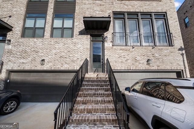 view of exterior entry featuring a garage, concrete driveway, and brick siding