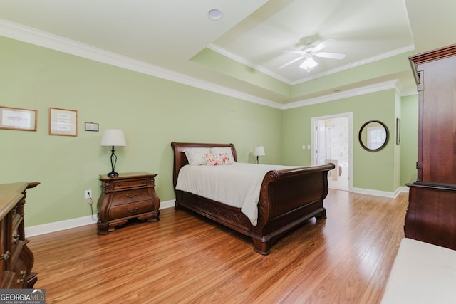 bedroom with a raised ceiling, ensuite bath, light wood-type flooring, and crown molding